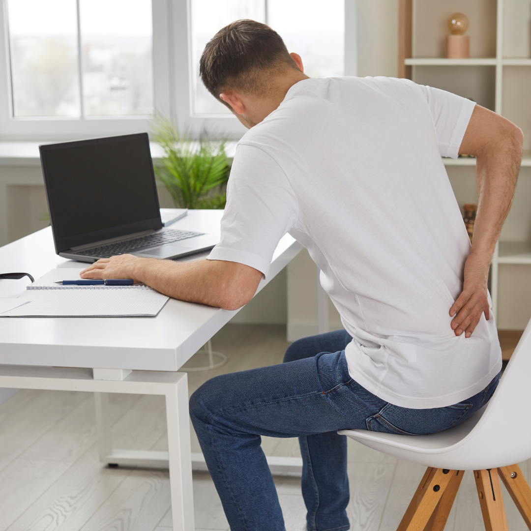 image of man at desk touchig back wondering about common back pain causes and proper back pain treatment